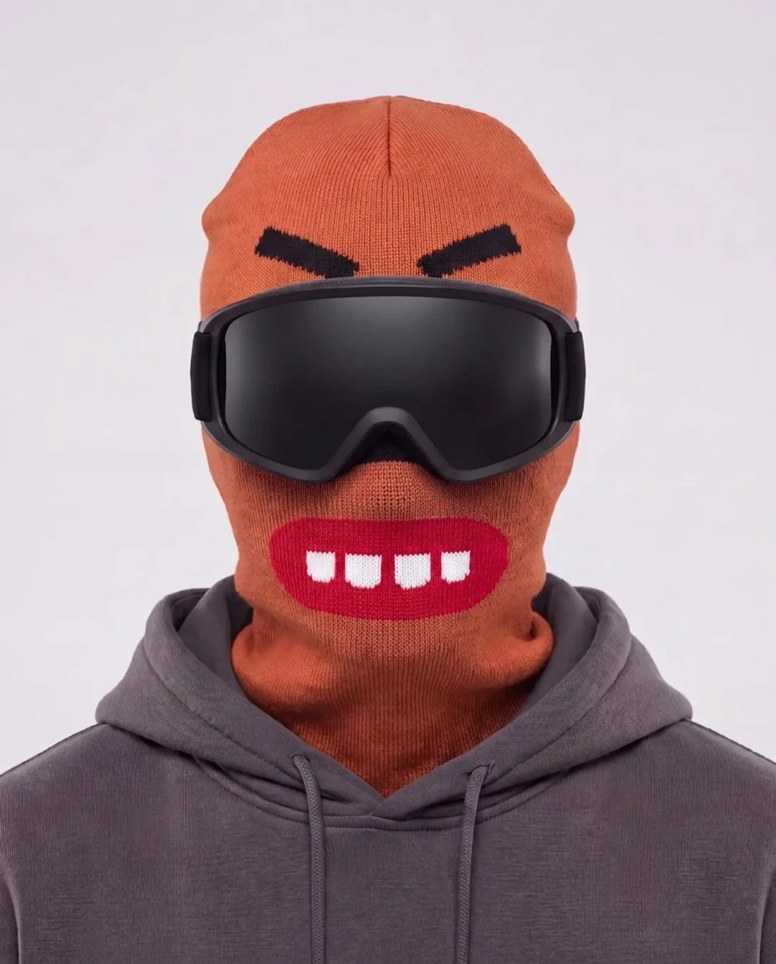 CHOMP orange character ski mask, front studio view, angry brows and red toothy grin, worn with black-lens ski goggles